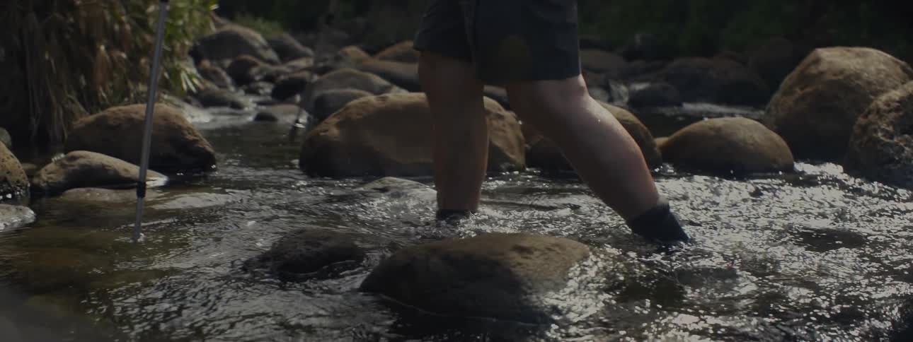Person wades in a flowing stream using walking sticks