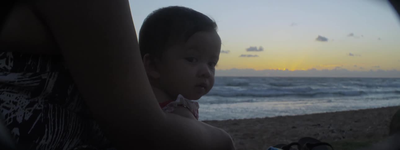 Adult holding a baby at the beach at sunset
