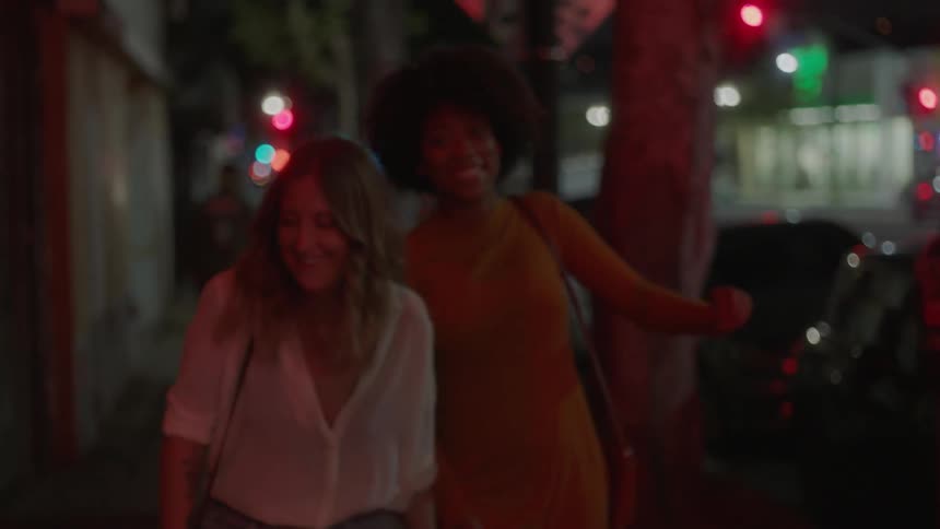 Two women walk out of a building smiling and holding hands