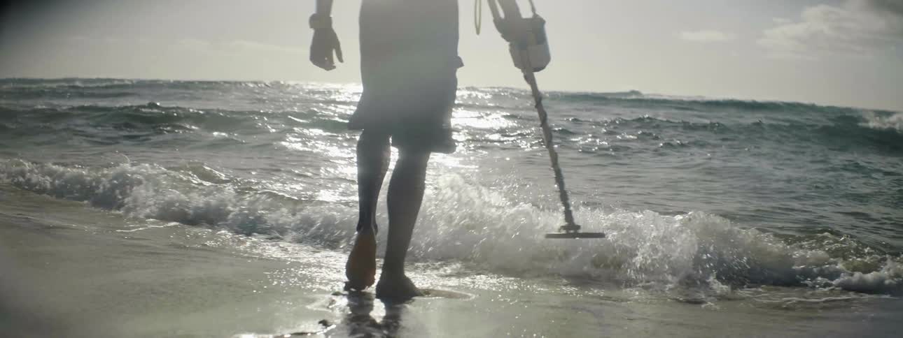 A man uses a metal detector on the beach