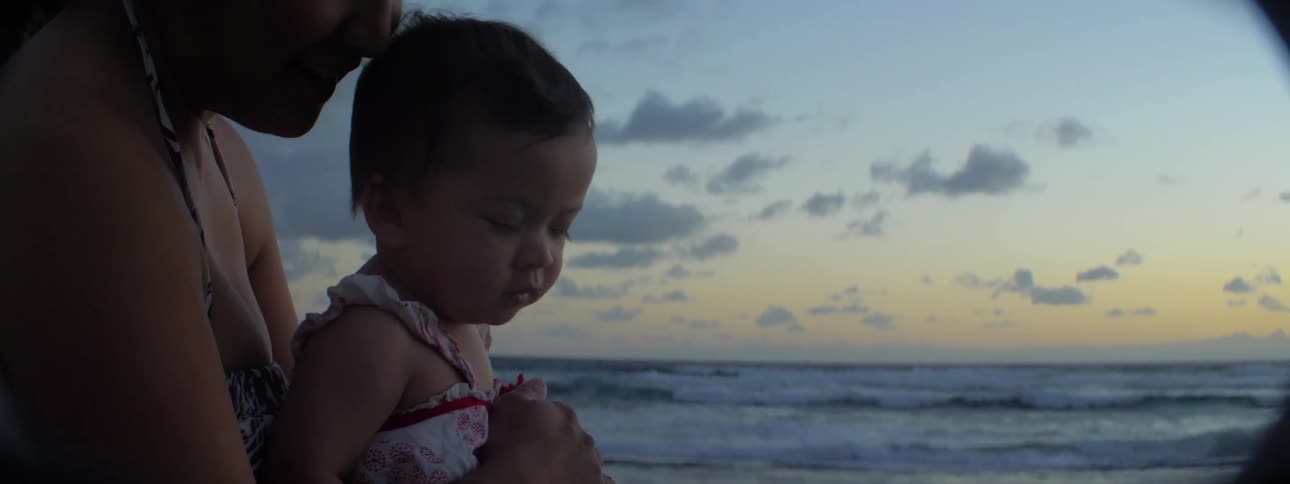 Adult holds a small child at the beach at sunset