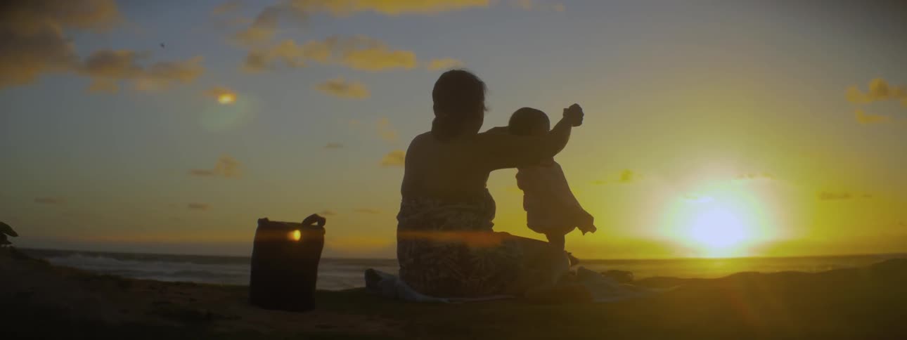 A woman holds a baby on the beach at sunrise