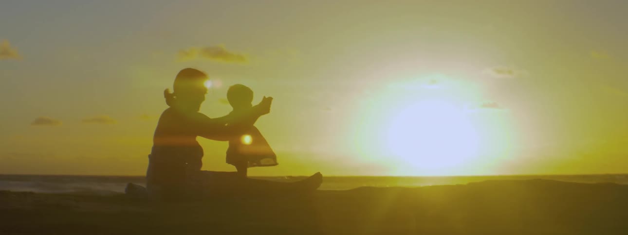 Woman and child sitting on the beach at sunset