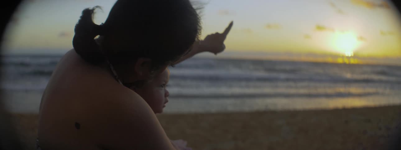 A woman holds a baby on the beach at sunset