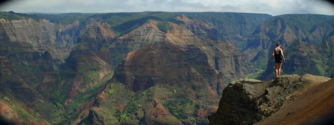 The high mountains are green, and a woman is perched near the edge