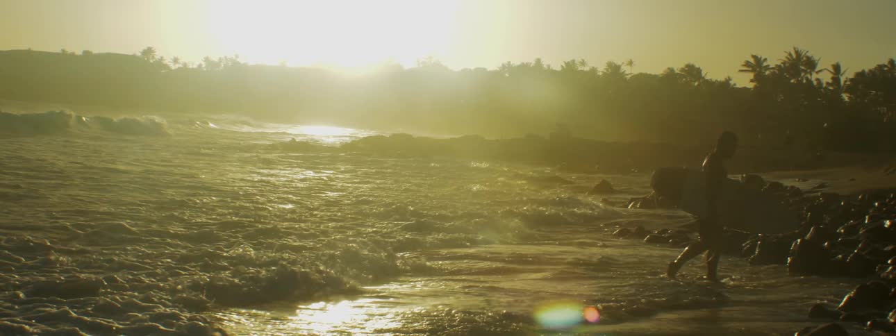 Person carries surfboard out of large splashing waves