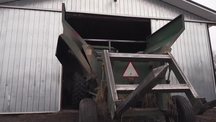 A hay baler pulls out of a barn