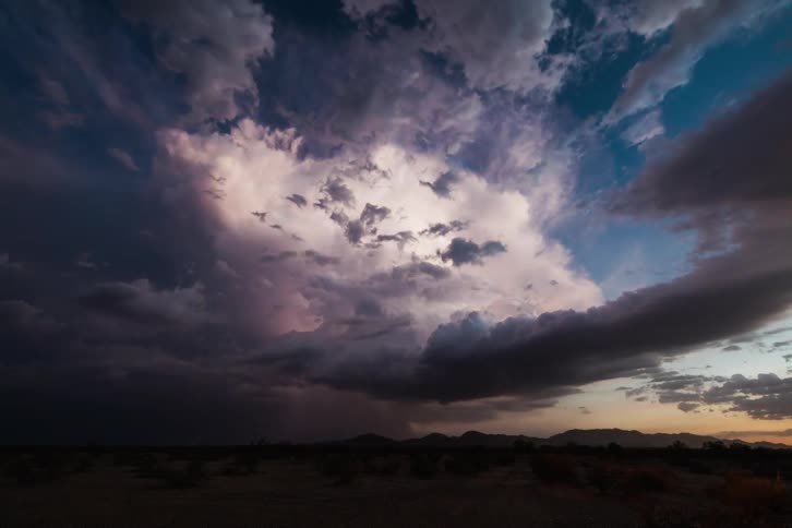 A storm swirls above a scrubby plain