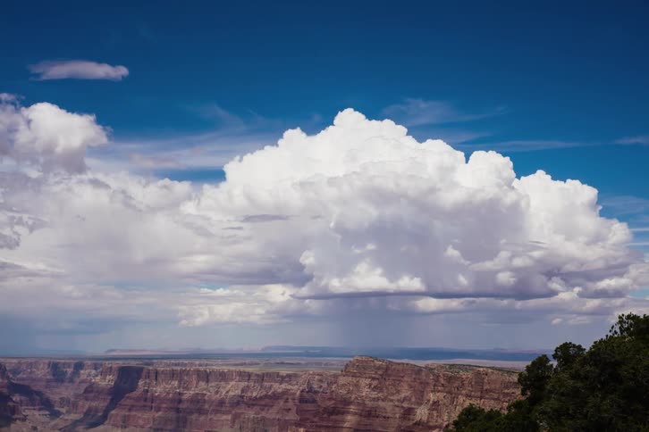 A view of some white clouds billowing in the sky over a mountain area