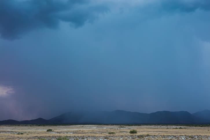 Storm clouds and lighting move over hills and the desert