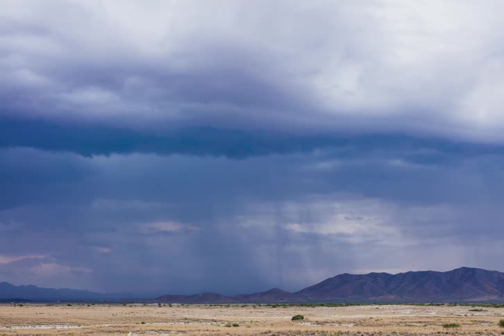 A huge storm cloud is pouring rain over the valley