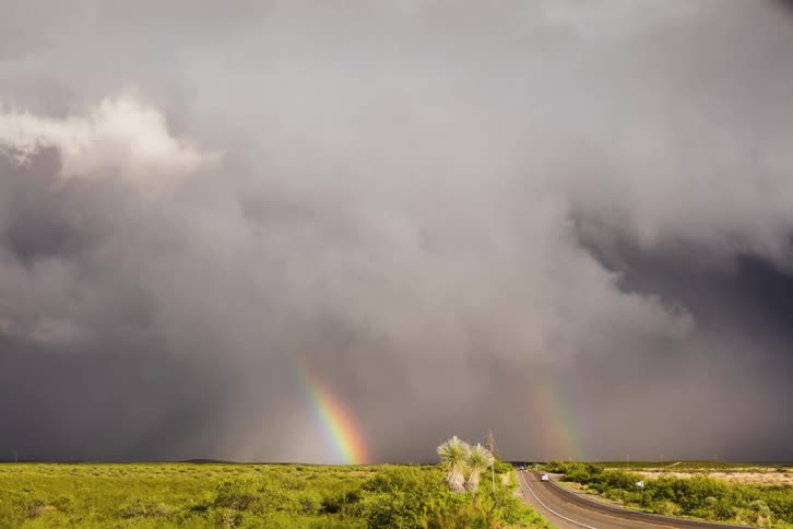 A storm builds over a field and then a rainbow appears
