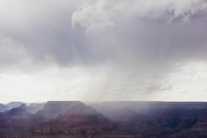Storm clouds move across and drop rain over a canyon