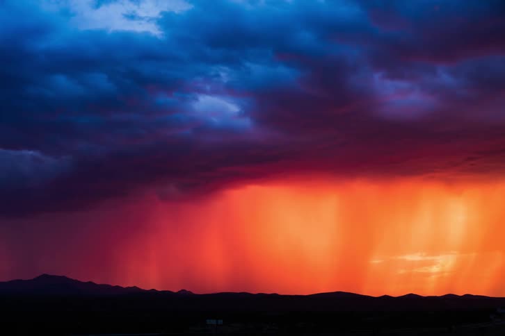 Storm clouds form and drop rain over hills at dusk