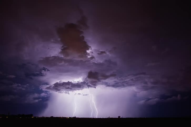 The night sky has clouds flashing with lightning