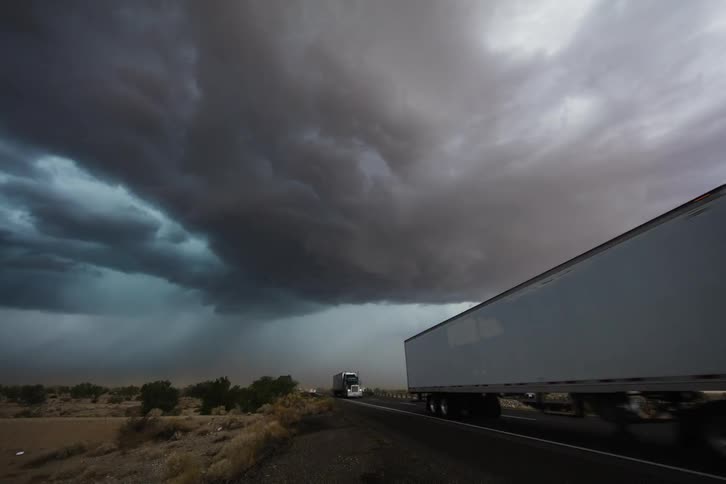 A storm cloud is in the distance of this busy highway