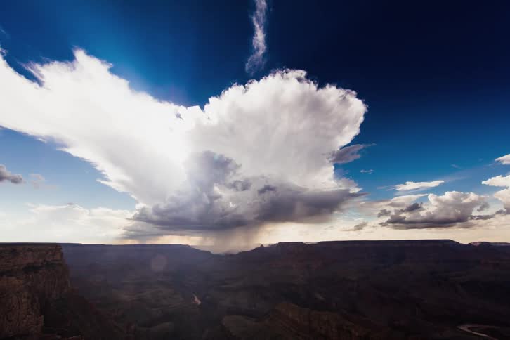 Clouds roll over a large canyon as the sun sets