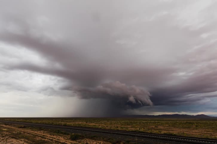 Storm clouds swirl and drop rain over a plain