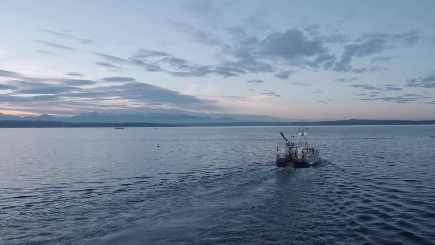 A fishing trawler leaving harbor in calm waters under a beautiful sunset sky