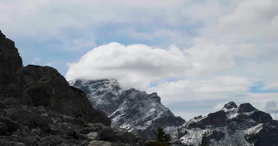 Clouds roll over jagged, snow-dusted mountain peaks