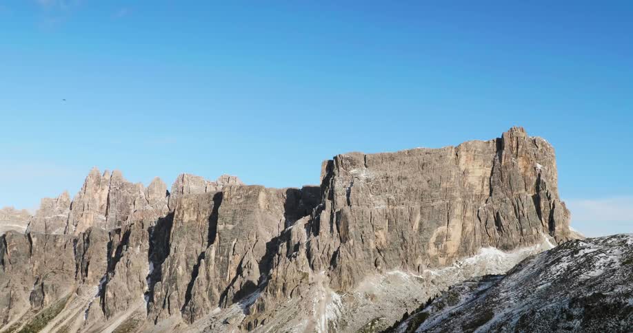 A bird flies high above craggy cliffs in a mountain range