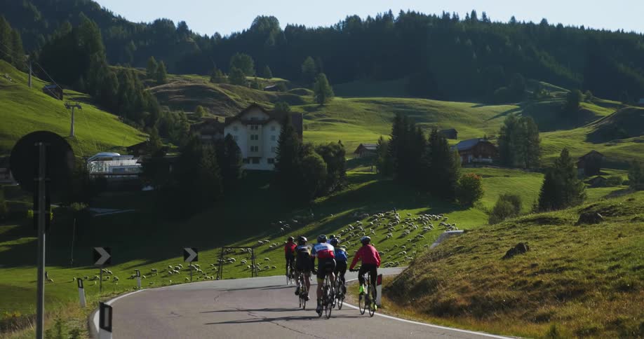 Bicyclists and vehicles travel along a winding road in an alpine village