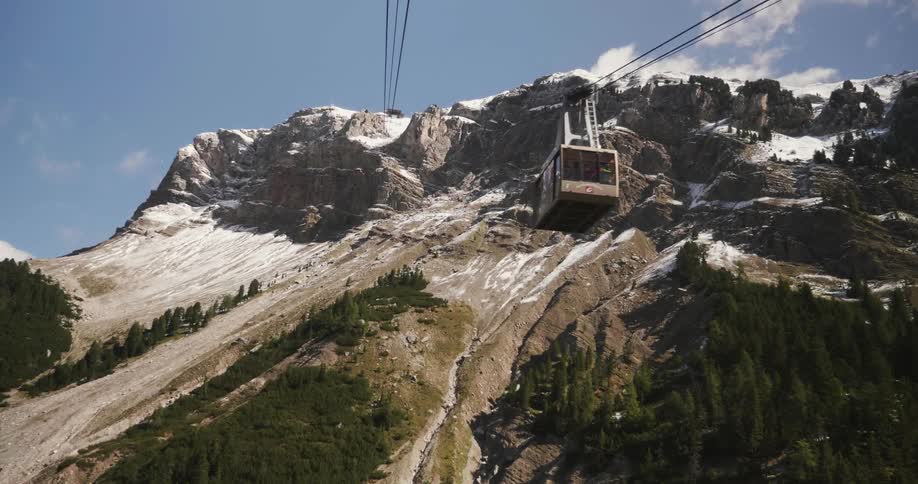 An aerial tram moves down the cable line near a rocky mountain peak