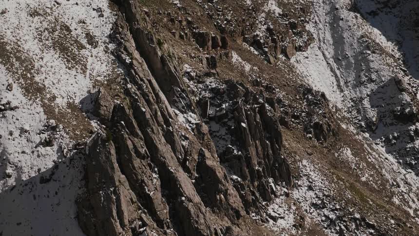 Snow dusts the steep slopes of a mountain during the day