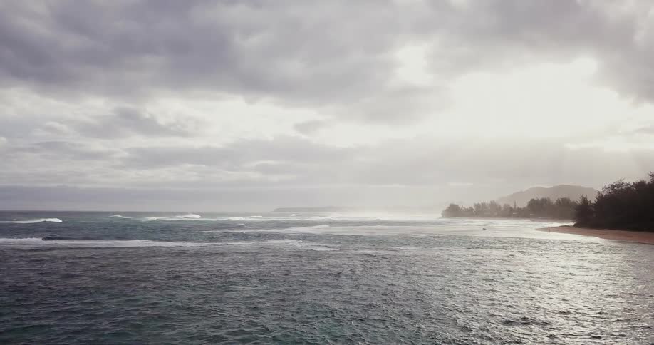 Gray clouds hang over a hazy shoreline as waves roll toward the beach