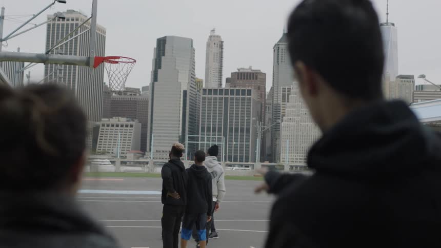 A man and woman spectate as a group of men play basketball