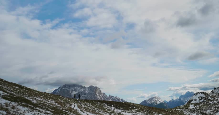 Two women are hiking on a snow-dusted hill on a cloudy day