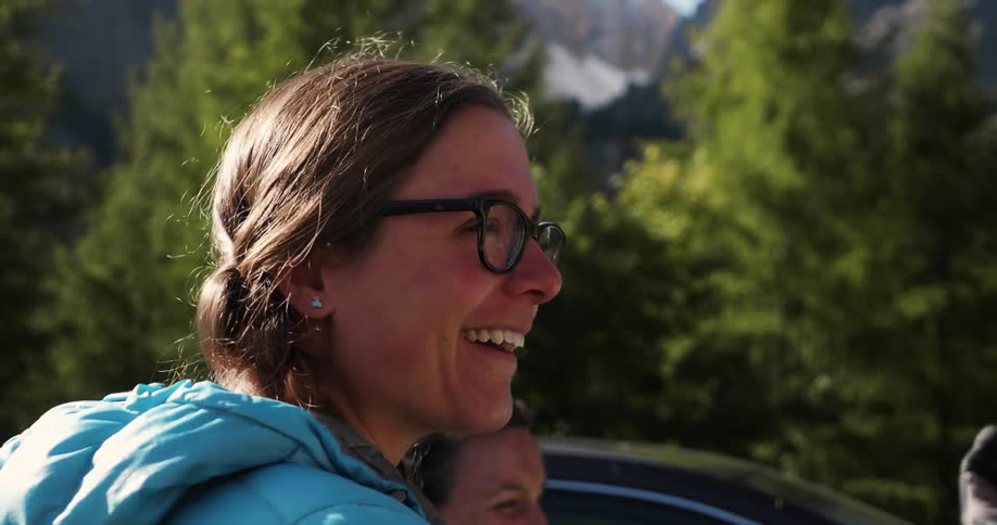 Smiling woman laughs and talks to a person by trees and mountains