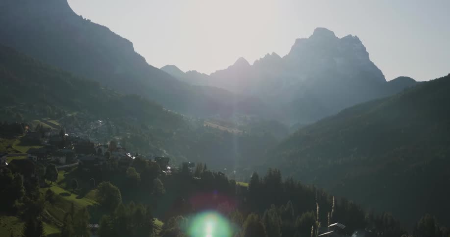 The sun shines brightly over a village nestled in a mountain valley