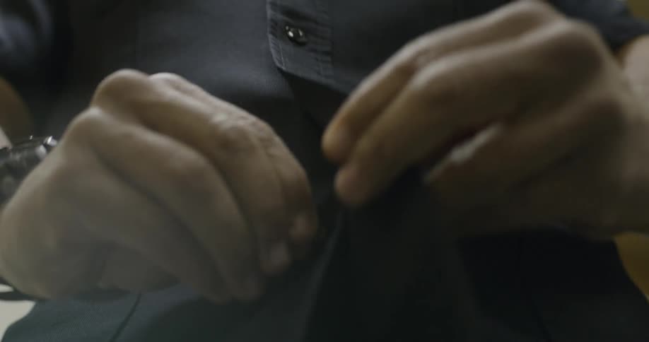 Close up of a man buttoning a black shirt