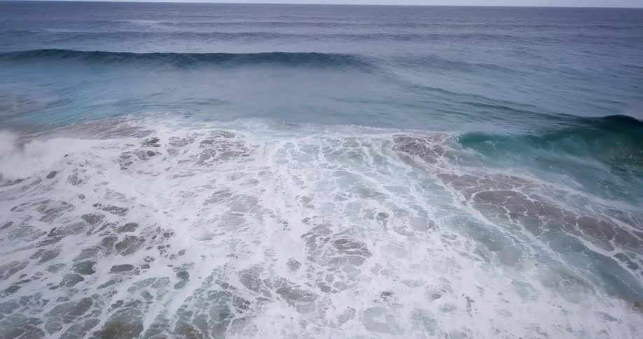 Bluegreen ocean waves roll into whitecaps crashing against the shore