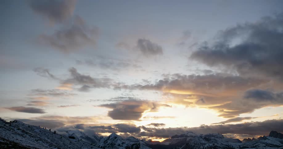 Clouds move across snow-dusted mountain peaks at sunrise