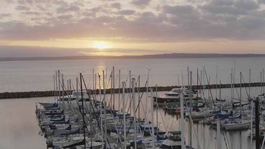 Flying through the masts of many sailboats docked at a marina as the sun sets in the distance
