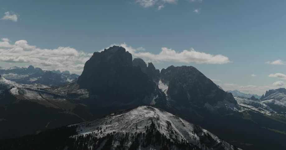 White clouds drift toward tall mountain peaks dusted with snow