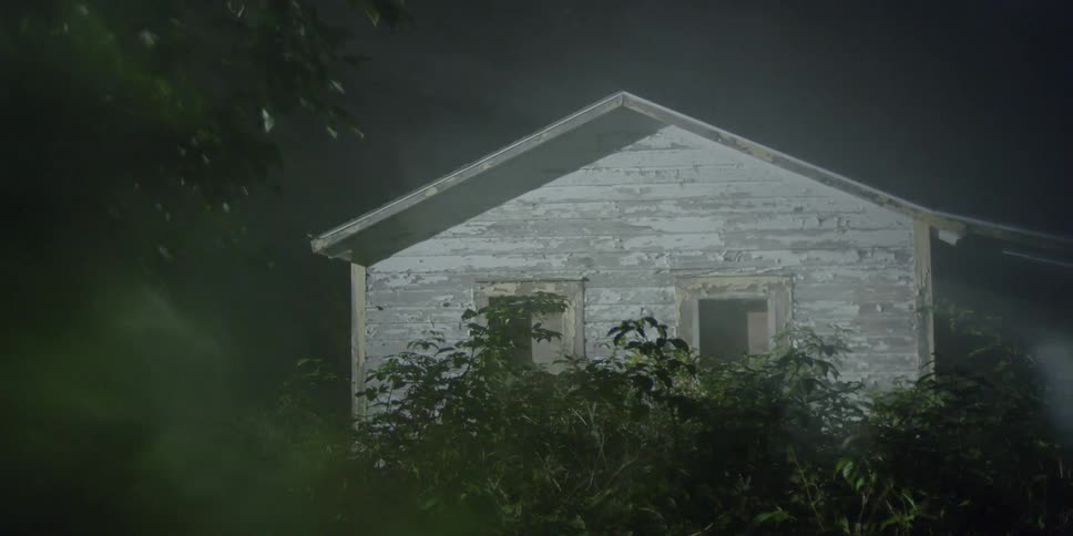 A bright light passes across a dilapidated building at night