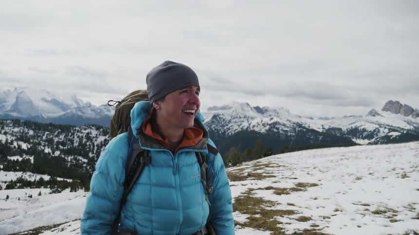 A woman wearing a backpack smiles as she looks at the mountain