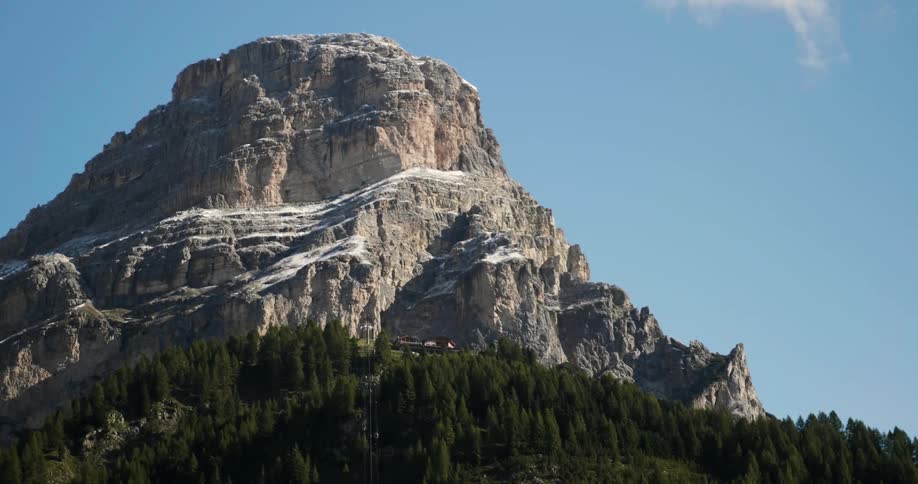 A wispy cloud moves in the sky near a snow-dusted mountain peak