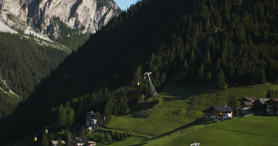 Gondolas move up and down the mountain over green grass and buildings