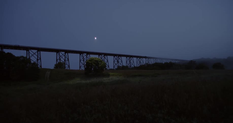 The moon looms over a bridge in a natural setting at night