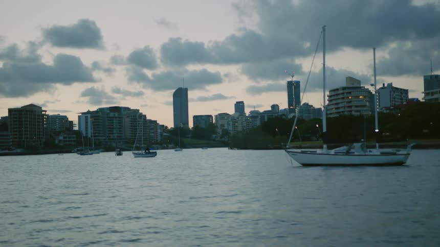 Sail boats sit tied at anchor in a city's harbor