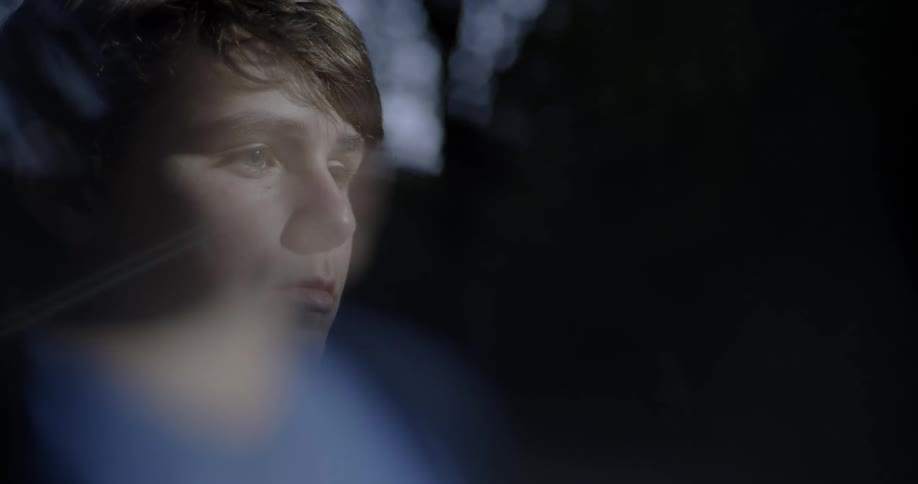 A teen boy is staring and blinking outside at night