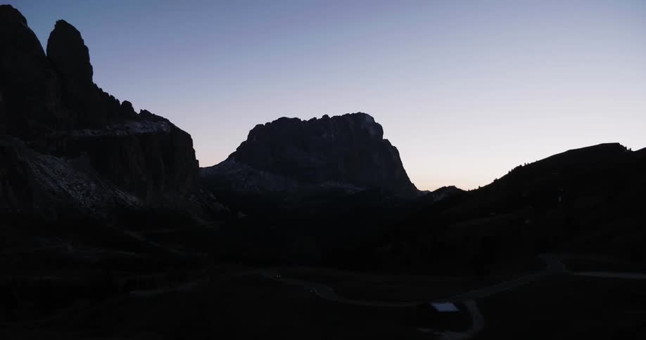 A car drives past a cabin in a mountainous area at dusk