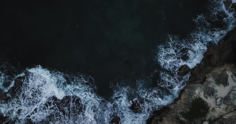 Aerial view of water hitting the side of a large rock or mountain