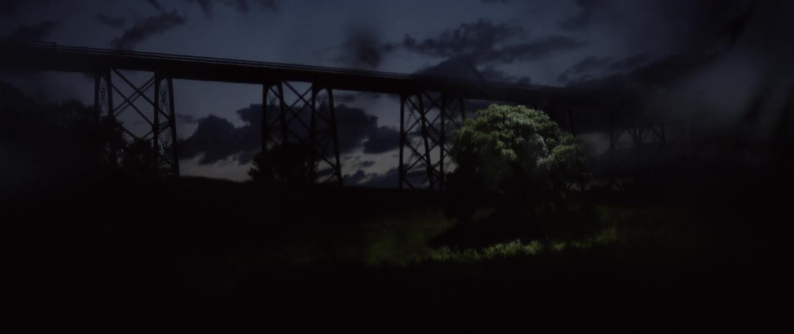 Trees obscure the view of a bridge as dusk fades