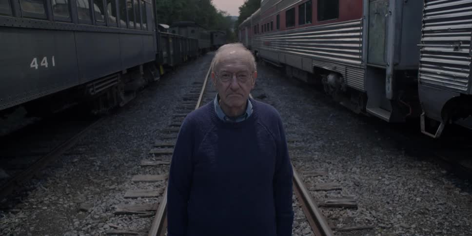 An elder man standing on train tracks between two trains