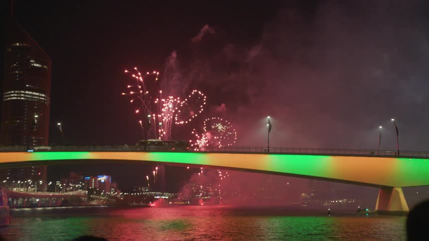 Tourists on a boat take pictures of fireworks on a river at night